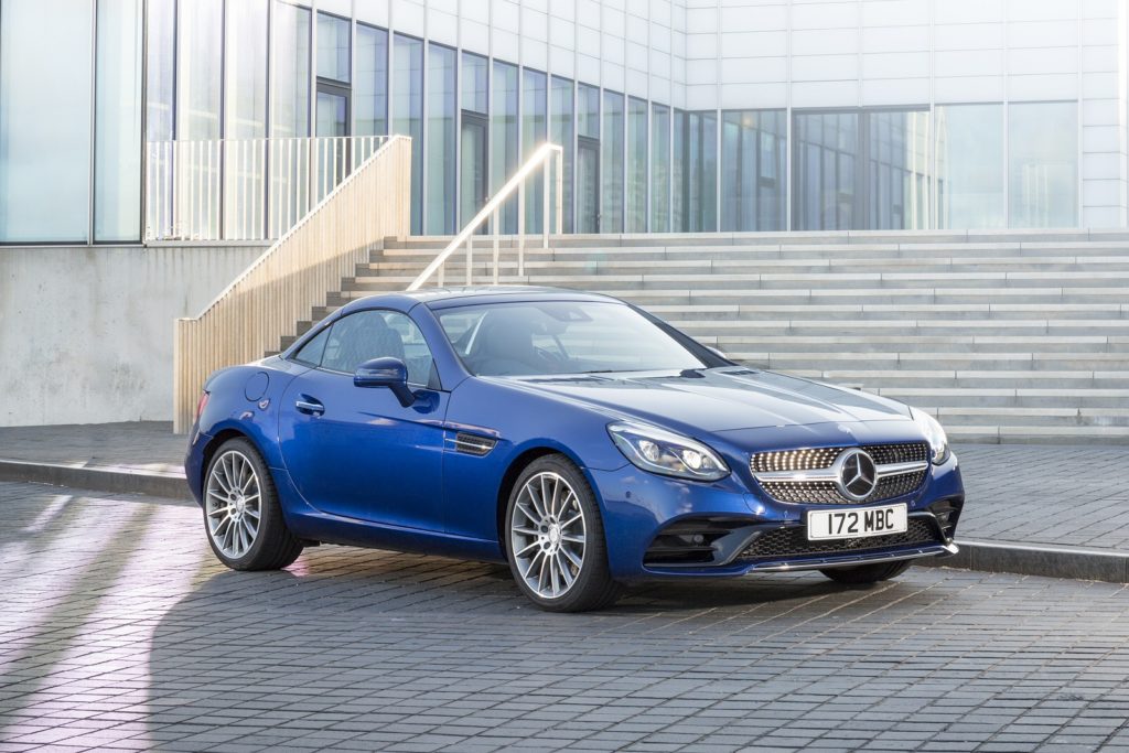 a blue mercedes SLC roadster parked on brick road in front of a modern building