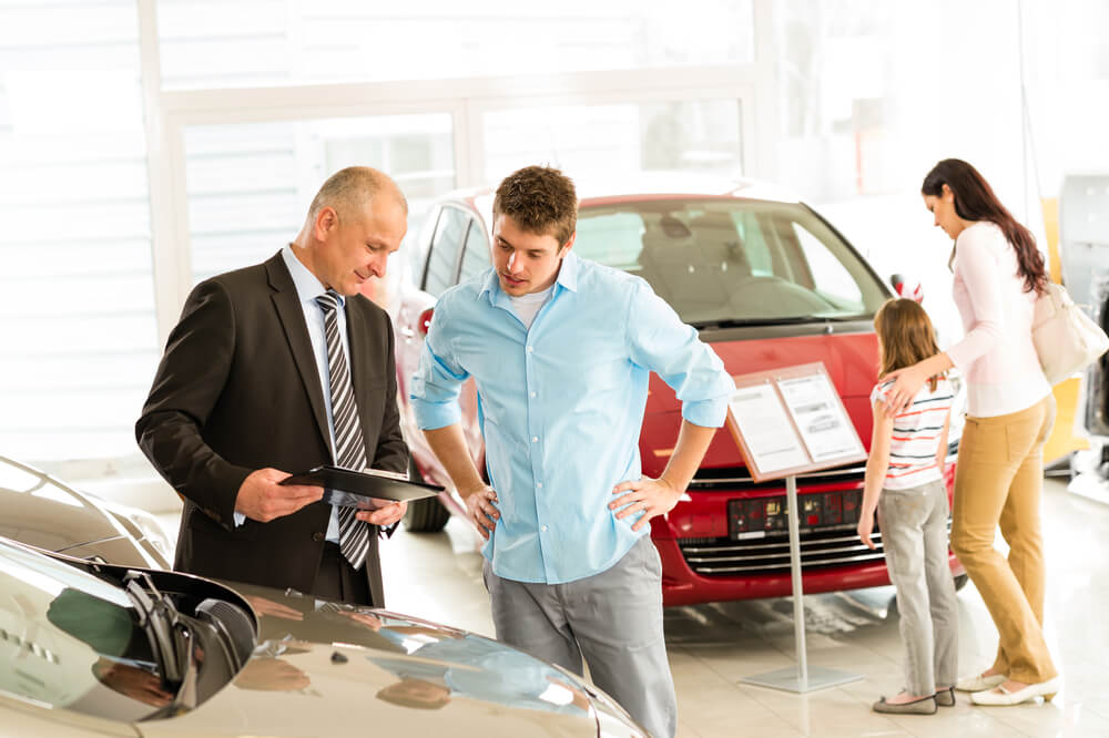 family looking at cars in the dealership with man talking to the car salesman