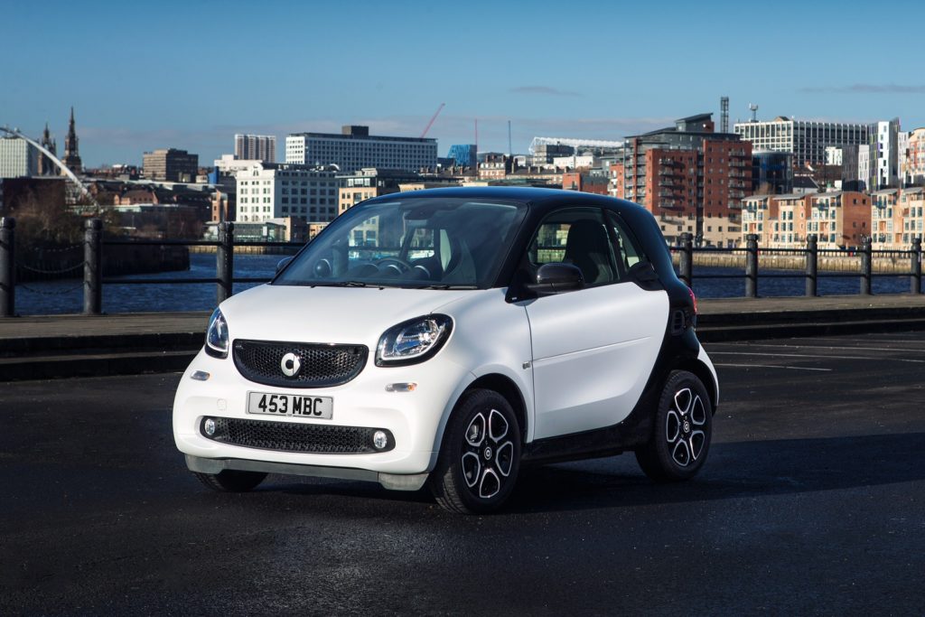 White Smart fortwo on a road with the city in the background