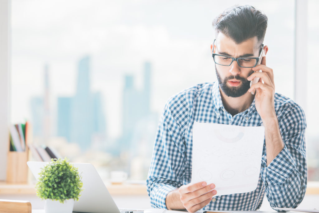 man in a checked shirt with glasses and a beard on the phone