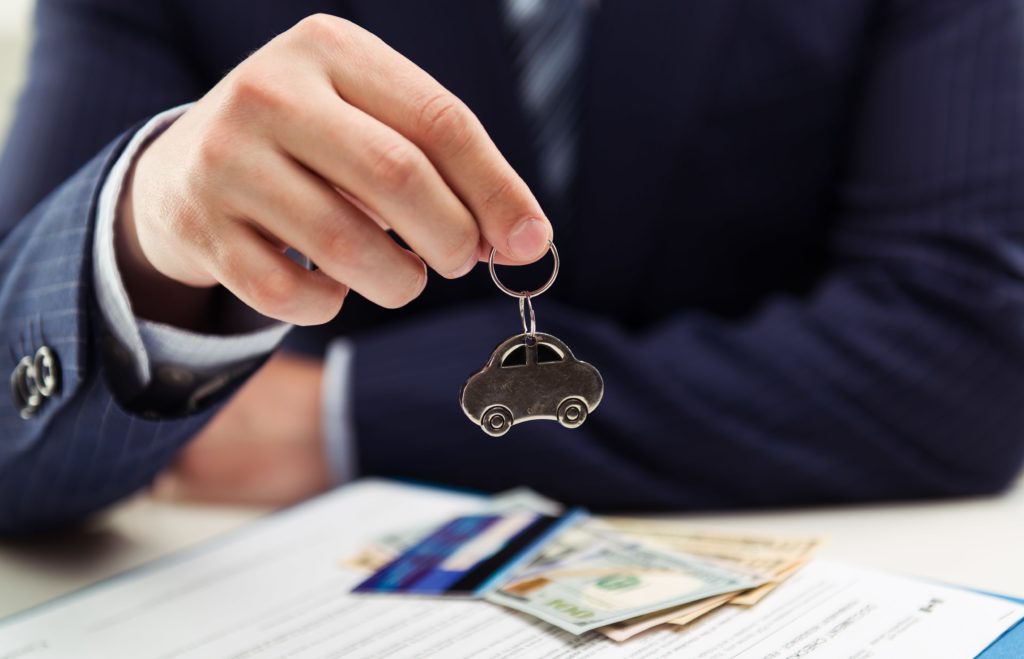 business man in blue suit holding car key ring over car leasing documentation