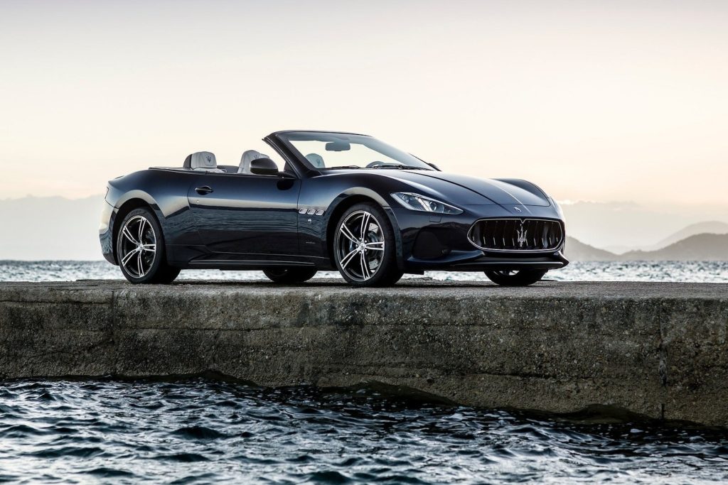 dark colouerd Maserati GranCabrio Convertible parked on concrete dock with sea below