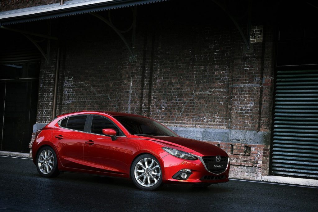 bright red mazda 3 hatchback parked next to bricked building