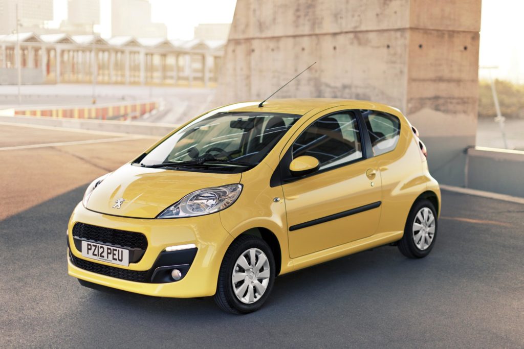 Yellow Peugeot 107 parked with a building in the background