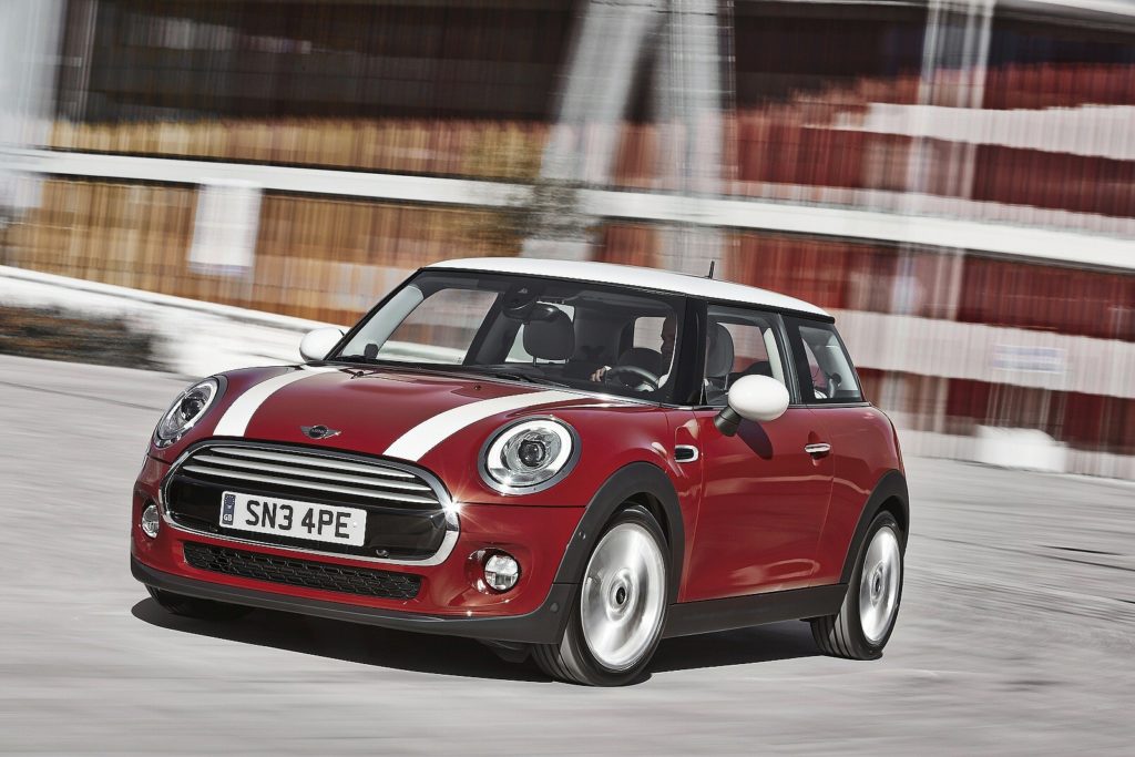 dark red mini hatchback driving on tarmac road with blurred buildings in the background