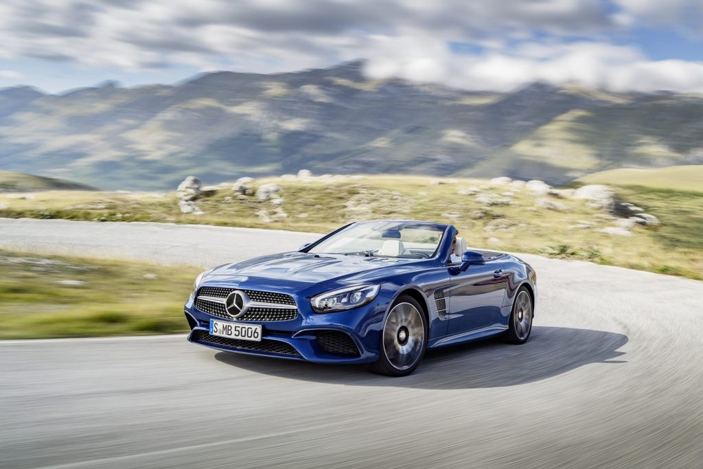 metallic blue mercedes-benz sl class convertible driving on tarmac road with green mountains blurred in the background