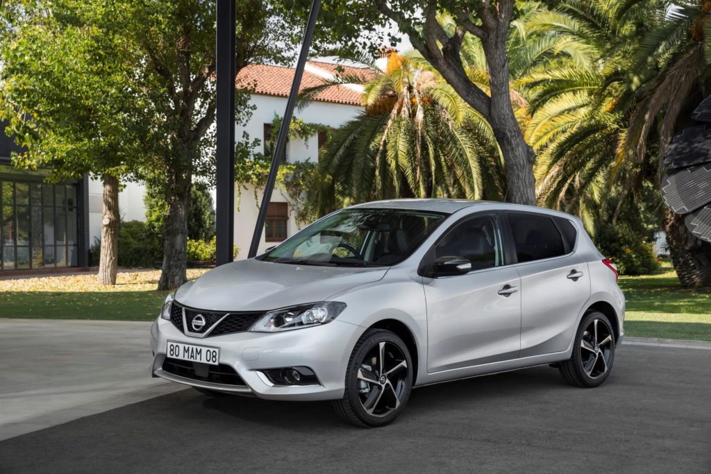 a silver nissan pulsar hatchback parked on tarmac with tropical background