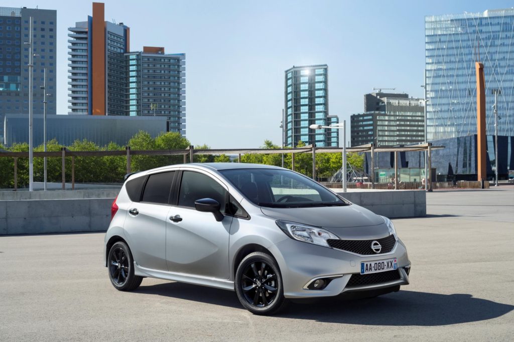 metallic nissan note parked on tarmac with city setting in the background