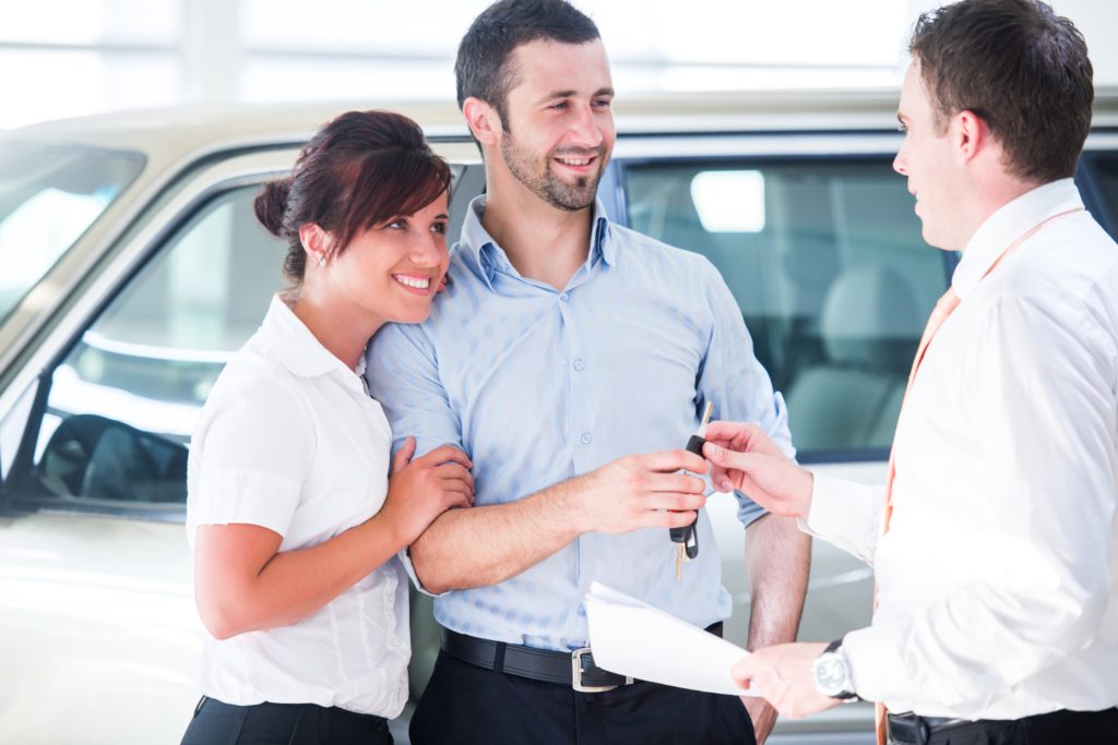 Young couple talking to sales guy about purchasing their new vehicle.