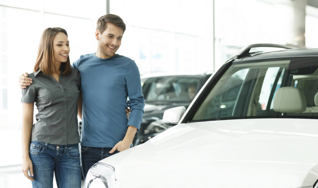 Couple looking and smiling at white car.