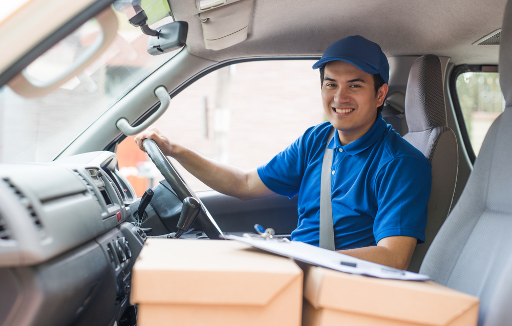 delivery man in a van with boxes on the passenger seat wearing a blue uniform and a blue cap