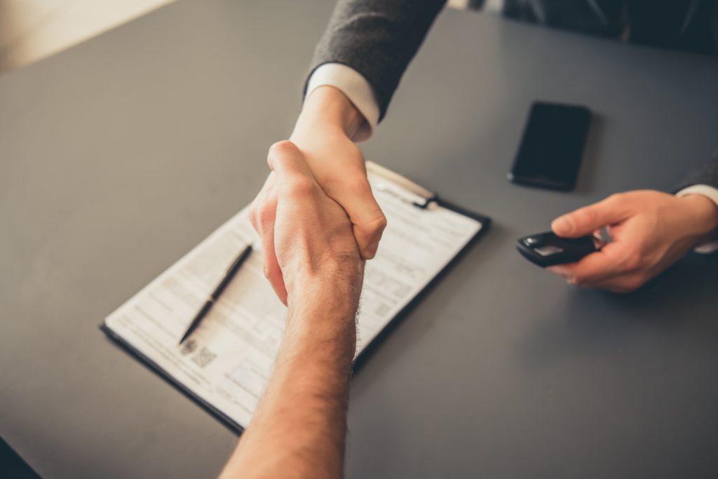 Visiting car dealership. Men are shaking hands while signing documents