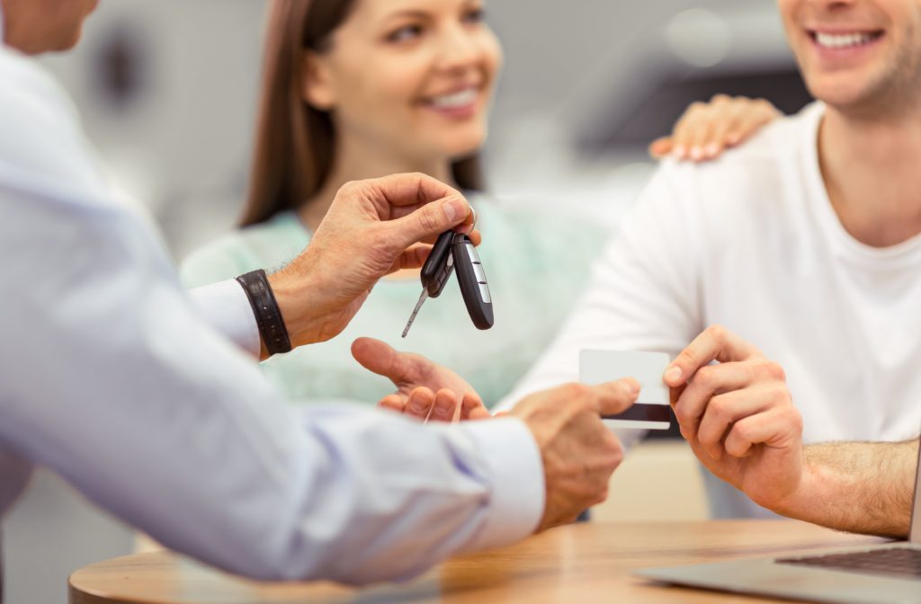 Young couple is smiling while buying a car, middle aged worker of a motor show is giving keys, close-up