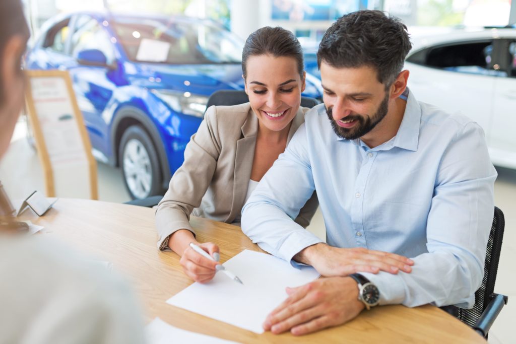 Young couple with car dealer in auto salon