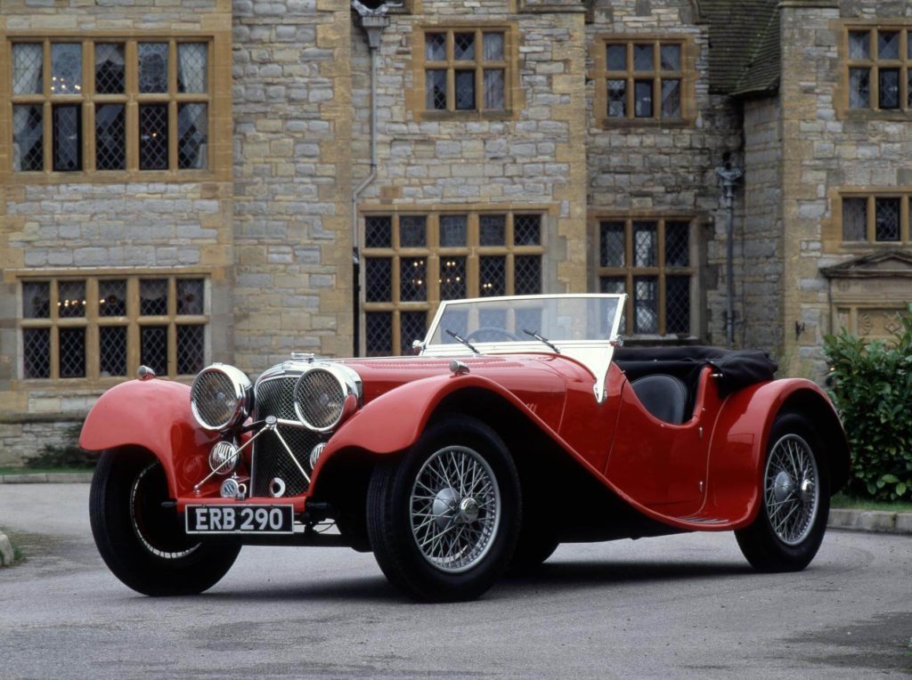 Jaguar SS100 in red parked outside an old building