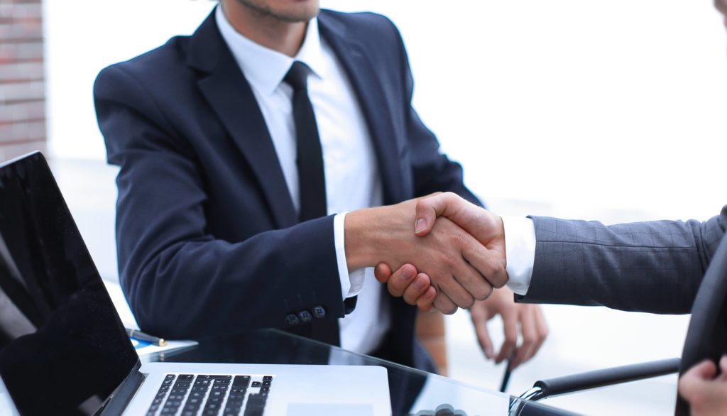 handshake business partners in front of the open laptop