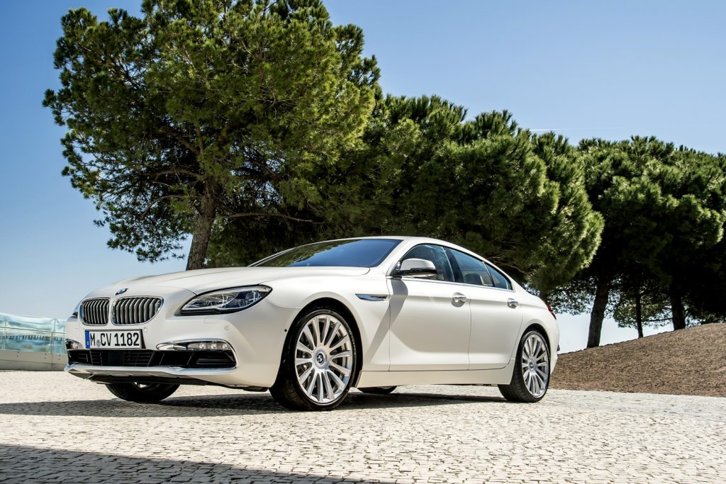 a white bmw 6 series gran diesel coupe parked on gravel with bright green trees in the background