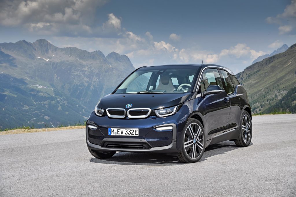 a dark coloured BMW i3 Rex parked on gravel with mountains in the background