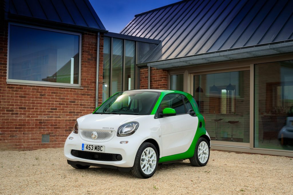 a white and green smart fortwo ed parked on gravel infront of small house